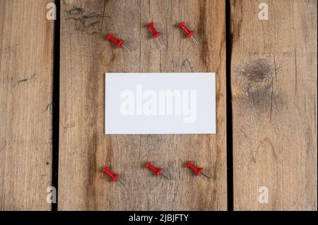 Une carte de visite vierge et des punaises rouges sur fond en bois. Un rectangle en papier blanc et six punaises se trouvent sur les anciennes planches fissurées. Sél Banque D'Images