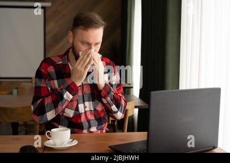 attention sélective de l'homme d'affaires éternuant dans les tissus tout en regardant l'ordinateur portable dans le bureau à domicile ou le café, indépendant allergique ou la grippe Banque D'Images