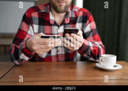 gros plan hommes mains tenant un téléphone mobile est de taper les détails de la carte pour faire un paiement en ligne tout en étant assis dans un café, avec une carte de crédit et un téléphone Banque D'Images
