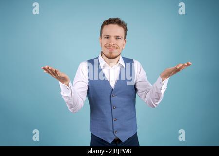 Ouah, c'est incroyable. Choqué homme d'affaires caucasien souriant pointant de côté geste dans l'espace de copie portant une chemise blanche et un jet bleu sur fond bleu Banque D'Images