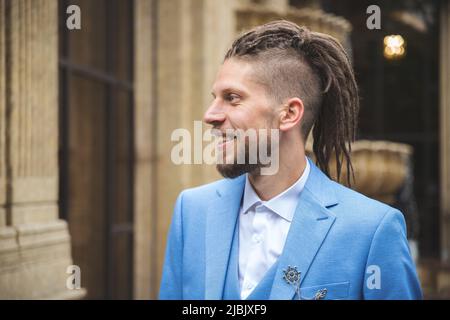 Jeune homme caucasien souriant avec des dreadlocks en costume bleu d'affaires, portrait d'extérieur Banque D'Images