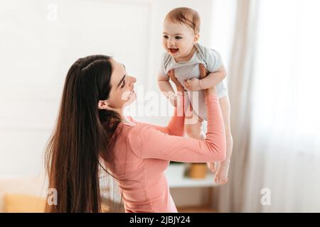 Jeune mère élevant heureux adorable bébé fille, tenant enfant faisant semblant de voler, d'avoir du plaisir et de jouer ensemble Banque D'Images
