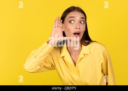 Curieuse femme millénaire à l'écoute des secrets qui se posent sur fond jaune Banque D'Images