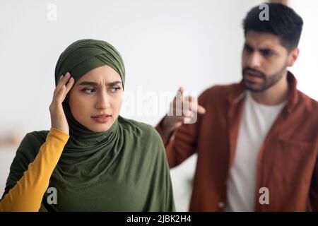 Un mari musulman en colère criant à une femme malheureuse debout à la maison Banque D'Images