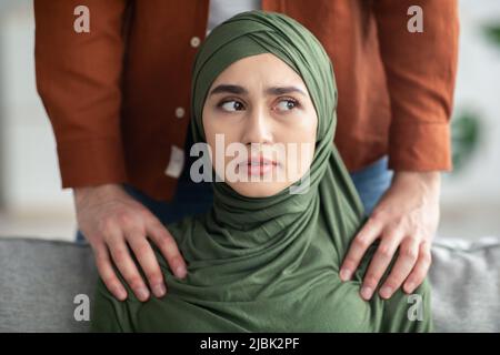 Un homme méconnaissable du Moyen-Orient touche les épaules d'une femme effrayée à l'intérieur Banque D'Images