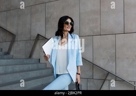 Belle jeune femme d'affaires avec un ordinateur portable dans ses mains marche vers le centre de bureau pour travailler, une réunion d'affaires, parler au téléphone, Banque D'Images