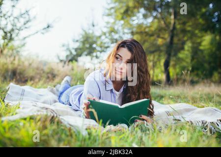 Belle jeune fille étudiante lit un livre, des études, allongé sur l'herbe dans la nature Banque D'Images