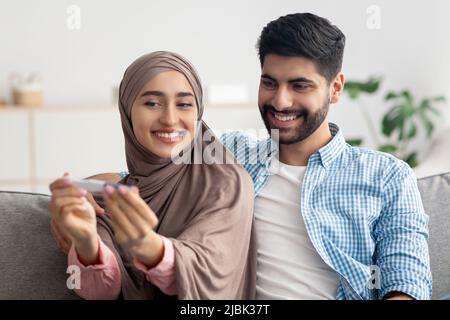 Joyeux époux musulmans tenant un test de grossesse positif célébrant le résultat à l'intérieur Banque D'Images