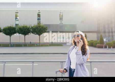 Jeune belle fille femme avec valise et téléphone, appelant quelqu'un, à la recherche d'appeler un taxi, à l'aéroport, est arrivée par avion, dans un ci inconnu Banque D'Images