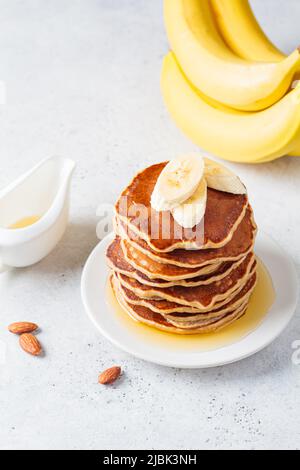 Pile de crêpes à la banane avec sirop sur une assiette blanche, fond gris. Concept de recette végétalienne. Banque D'Images