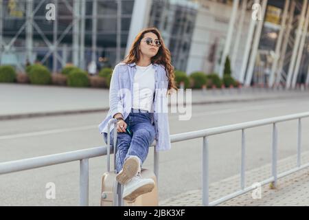 Jeune femme avec une valise dans la rue près de l'aéroport, de la gare, attendant à l'arrêt de bus, attendant un taxi Banque D'Images