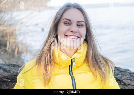 Portrait d'une jeune fille souriante et heureuse regardant dans l'appareil photo contre le fond d'un lac dans la forêt. Santé mentale. Femme portant un jaune vif Banque D'Images