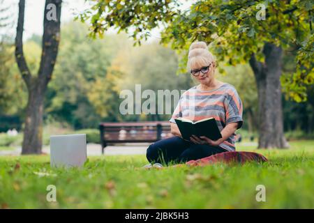 Belle femme blonde séchée sur l'herbe dans le parc lit un livre, des études, des sourires, des repose Banque D'Images