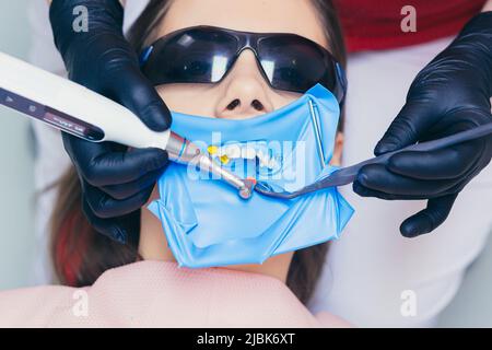 Gros plan un dentiste avec un assistant traite les dents de la femme, le visage du patient est fermé Banque D'Images