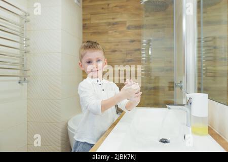 Un petit garçon lave ses mains avec du savon, désinfecte dans la salle de bains, à la maison, au restaurant, à l'hôtel, au centre commercial Banque D'Images