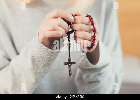 Gros plan photo des mains pliées d'une jeune femme tenant un rosaire, priant Banque D'Images