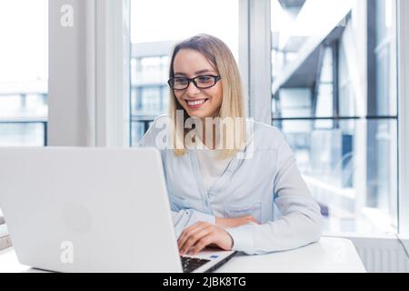 Caucasien jeune femme pigiste heureuse assise à table et parlant en ligne sur webcam à distance. Une étudiante parle et communique un appel vidéo avec f Banque D'Images