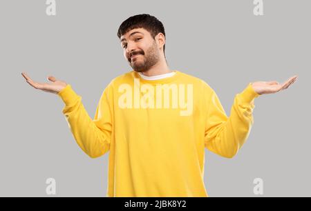homme confus dans le chandail jaune haussant Banque D'Images