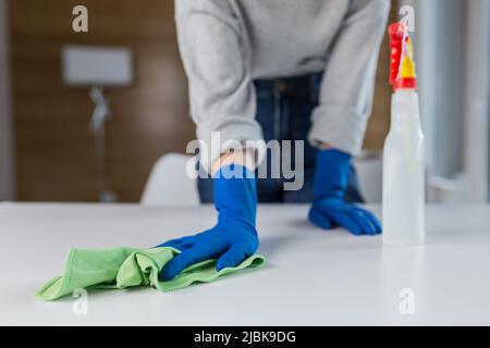 Gros plan des mains d'une jeune femme qui nettoie, lave la table avec un chiffon en gants de caoutchouc à la maison, au bureau, à l'hôtel Banque D'Images