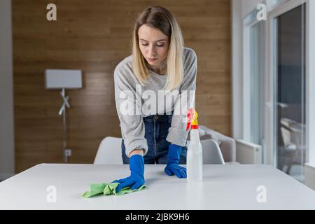 Une jeune femme nettoie, femme au foyer, lave la table dans des gants en caoutchouc à la maison, au bureau, à l'hôtel Banque D'Images