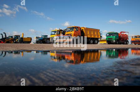 Voitures colorées. Souffleuse à neige. Grandes machines d'enlèvement de neige à l'aéroport. Équipement routier. Niveleuse, camion à benne basculante, tracteur. Une nouvelle voiture se reflète dans une flaque. Réflexion. Extérieur Banque D'Images