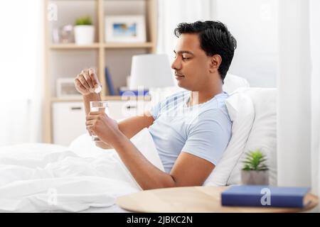 homme au lit tombant le médicament dans un verre d'eau Banque D'Images