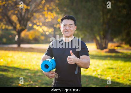 Des yogi masculins actifs et beaux se promène dans un parc en forêt avant ou après un entraînement. Un jeune athlète asiatique va à la classe de yoga avec un fitne Banque D'Images