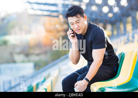 Un athlète appelle un médecin, un homme asiatique a blessé les muscles de la jambe pendant la course et l'entraînement du matin, s'est posé, a une douleur sévère Banque D'Images