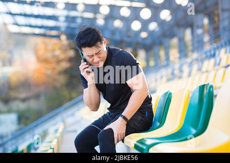 Un athlète appelle un médecin, un homme asiatique a blessé les muscles de la jambe pendant la course et l'entraînement du matin, s'est posé, a une douleur sévère Banque D'Images