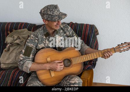 Vétéran du concept de jeu de guitare en fauteuil roulant. Réunion de famille. Fils et femme. Uniforme de camouflage. Contexte familial. Se reposer ensemble. Des sentiments qui se manifestent Banque D'Images