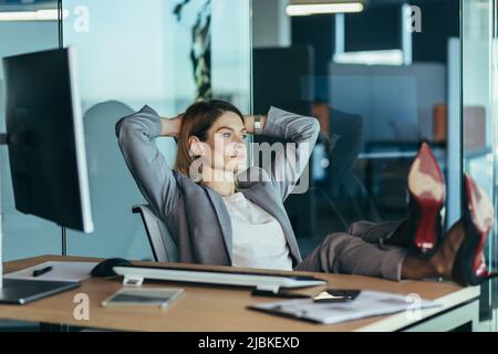 Femme directrice se reposant et rêvant au travail, femme d'affaires jetant ses mains derrière sa tête et les pieds sur la table, se reposant sur la journée de travail Banque D'Images