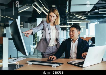 Une femme patron pointe vers un collègue de montage sur un moniteur d'ordinateur, des gens d'affaires travaillant sur un projet dans un bureau moderne Banque D'Images