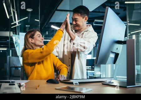 Deux employés à succès, un homme asiatique et une femme travaillant au bureau à l'ordinateur, célébrant la victoire et le succès ensemble, applaudissant leur han Banque D'Images