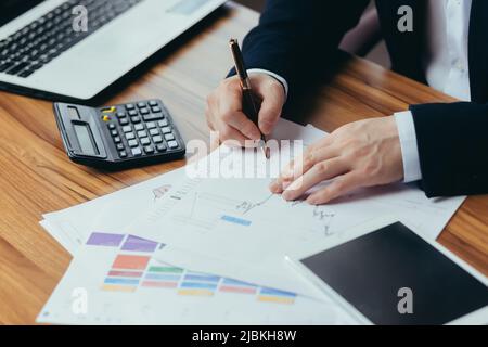 Gros plan des mains d'un jeune homme comptable, homme d'affaires, directeur travaille avec des documents, compte sur une calculatrice, écrit des factures dans le bureau de la Banque D'Images