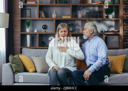 Couple senior à la maison, la femme a une douleur thoracique sévère et un essoufflement, le mari tente de calmer la femme Banque D'Images