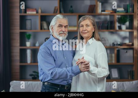 Heureux couple marié, homme et femme aux cheveux gris, souriant et regardant l'appareil photo, enserrant le portrait à la maison Banque D'Images