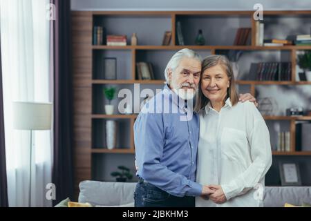 Heureux couple marié, homme et femme aux cheveux gris, souriant et regardant l'appareil photo, enserrant le portrait à la maison Banque D'Images