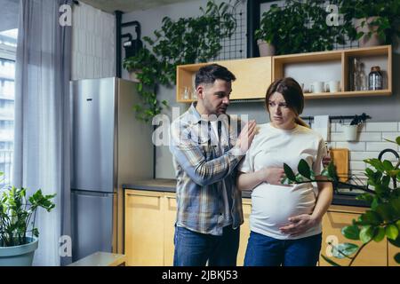 Jeune famille à la maison homme et femme enceinte, le mari rassure la femme après querelle dans la cuisine Banque D'Images