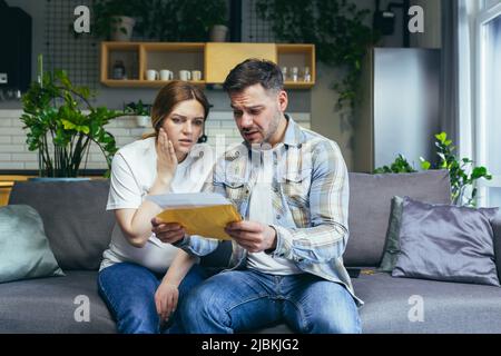 Un jeune homme de couple et une femme enceinte à la maison assis sur un canapé, frustrés et tristes, ont reçu une mauvaise lettre Banque D'Images