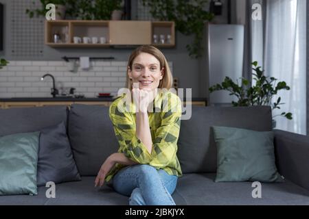 Portrait d'une femme d'âge moyen réussie, d'une femme au foyer assis sur un canapé dans la cuisine et souriant regardant l'appareil photo Banque D'Images