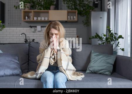 La femme malade est assise sur le canapé à la maison, a une toux et de la fièvre, le rhume et le nez qui coule Banque D'Images