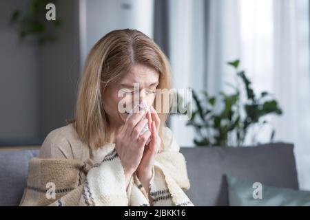 La femme malade est assise sur le canapé à la maison, a une toux et de la fièvre, le rhume et le nez qui coule Banque D'Images