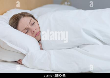 Photo en gros plan d'une femme endormie et contrariée, couchée au lit sous une couverture, essayant de s'endormir Banque D'Images