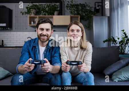 Couple heureux homme et femme jouant au jeu en utilisant le joystick tout en étant assis sur le canapé à la maison Banque D'Images
