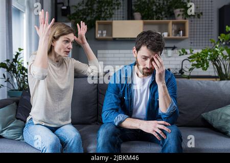 Querelle familiale, homme et femme assis sur un canapé à la maison. La femme en colère hurle à son mari, blames. L'homme est silencieux. Il écoute, tient sa tête, embarr Banque D'Images
