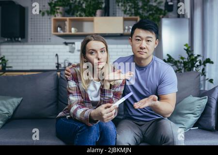Jeune couple à la maison frustré montrant négatif médecin test de grossesse, consultation de médecin en ligne, homme et femme ensemble à la maison essayant d'obtenir pregn Banque D'Images