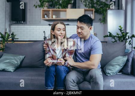 Jeune couple à la maison frustré montrant négatif médecin test de grossesse, consultation de médecin en ligne, homme et femme ensemble à la maison essayant d'obtenir pregn Banque D'Images