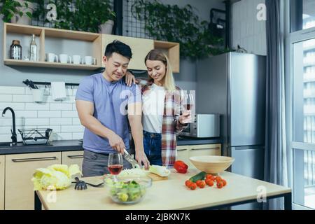 Jeune multiracial famille heureuse, asiatique homme et femme, se réjouir et cuire le dîner ensemble, couper les légumes pour la salade, couple heureux à la maison à une date dans lov Banque D'Images