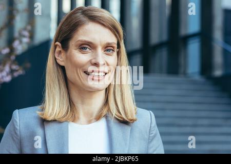Photo gros plan portrait d'une femme d'affaires blonde à l'extérieur du bureau, femme d'affaires regardant l'appareil photo et souriant Banque D'Images