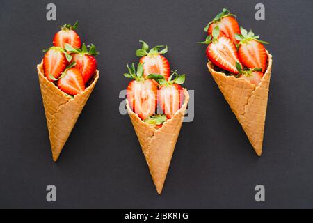 Vue de dessus des fraises mûres coupées dans des cornets de gaufres sur fond noir Banque D'Images